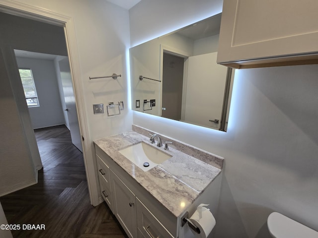 bathroom featuring parquet floors, vanity, and toilet