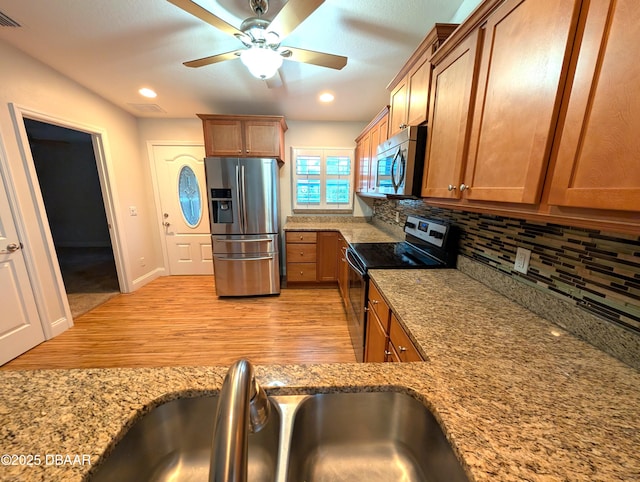 kitchen with stainless steel appliances, brown cabinetry, a sink, and backsplash