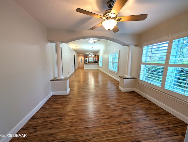 corridor with arched walkways, dark wood-style flooring, decorative columns, and baseboards