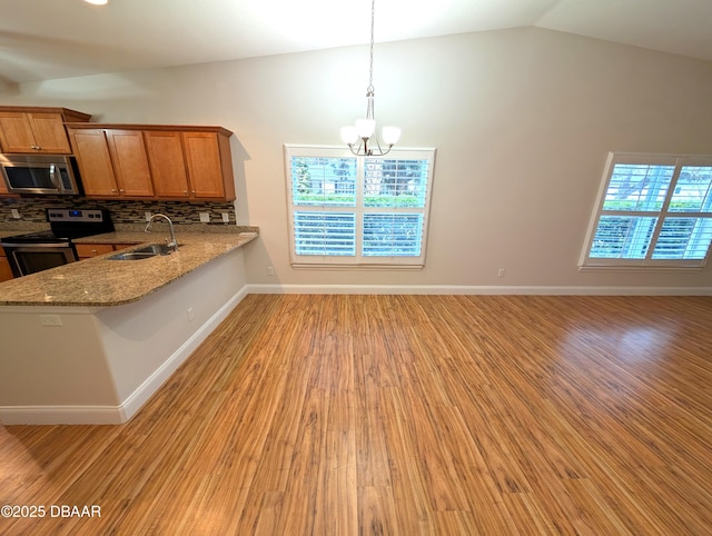 kitchen featuring stainless steel appliances, a peninsula, a sink, brown cabinetry, and pendant lighting