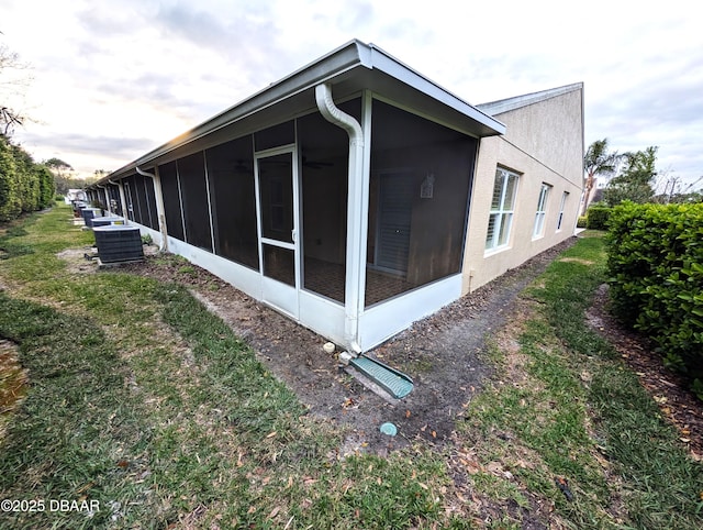 view of side of property with a sunroom, stucco siding, and central AC unit