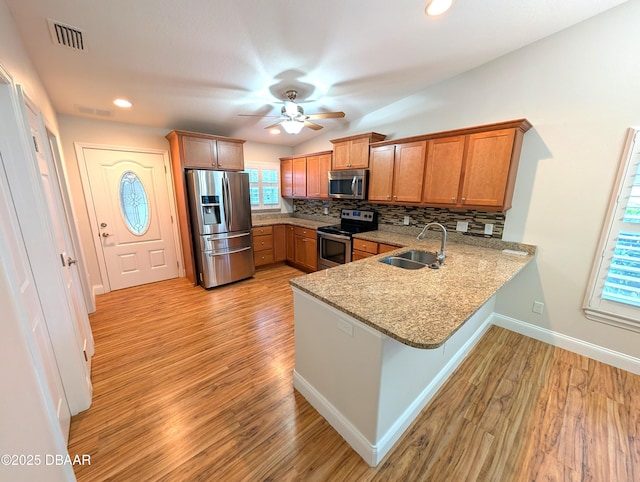 kitchen featuring brown cabinetry, decorative backsplash, a peninsula, stainless steel appliances, and a sink