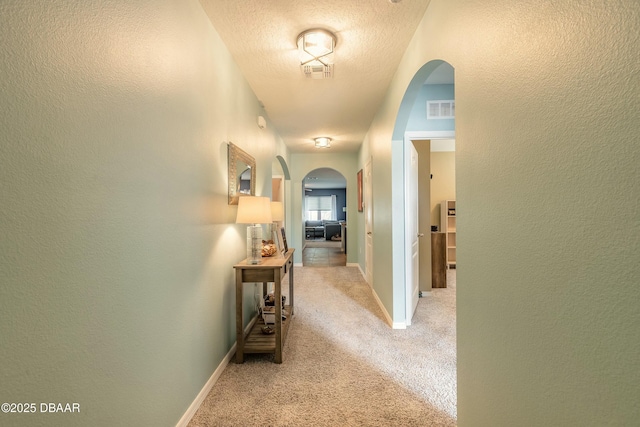 hall with light colored carpet, visible vents, arched walkways, and a textured ceiling