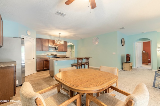 dining area featuring visible vents, ceiling fan, light carpet, arched walkways, and a textured ceiling