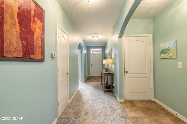 hallway with baseboards, arched walkways, a textured ceiling, and visible vents