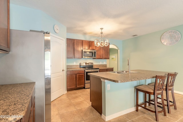 kitchen with a kitchen bar, a kitchen island with sink, a sink, stainless steel appliances, and light tile patterned floors