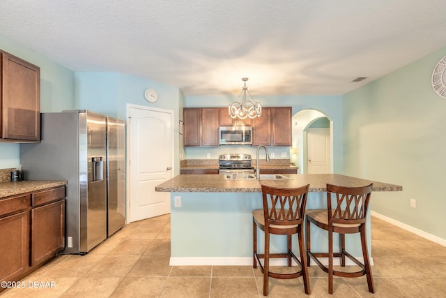 kitchen with a breakfast bar area, a kitchen island with sink, arched walkways, a sink, and appliances with stainless steel finishes