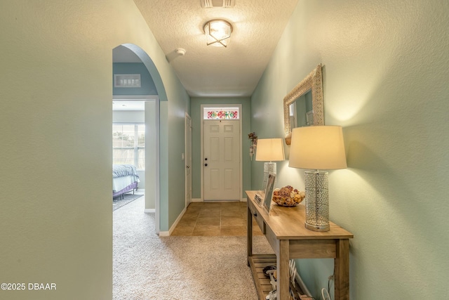 foyer entrance with visible vents, baseboards, light carpet, arched walkways, and a textured ceiling