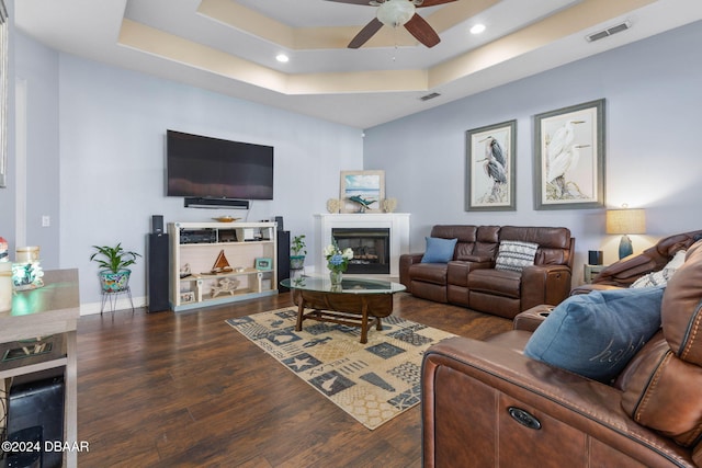 living room with a tray ceiling, ceiling fan, and dark hardwood / wood-style flooring