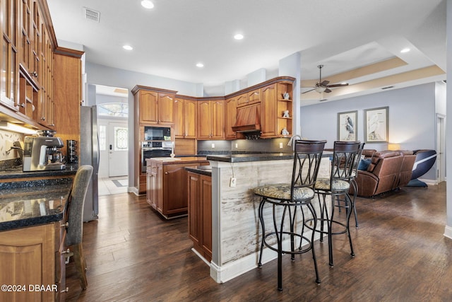 kitchen featuring ceiling fan, stainless steel appliances, a kitchen breakfast bar, dark hardwood / wood-style flooring, and kitchen peninsula