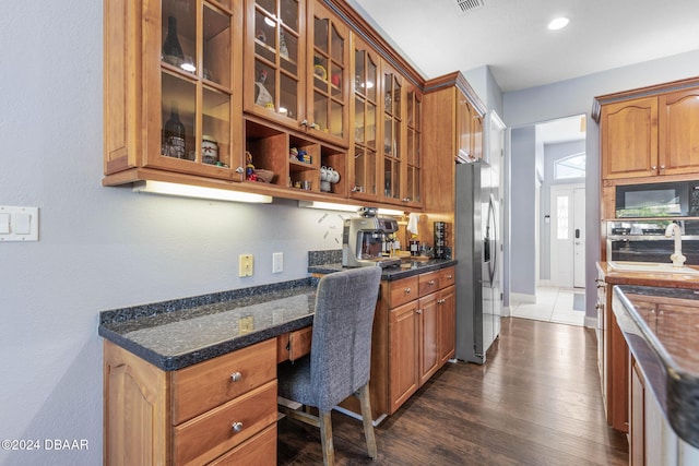 kitchen featuring dark hardwood / wood-style flooring, built in desk, stainless steel appliances, and dark stone counters