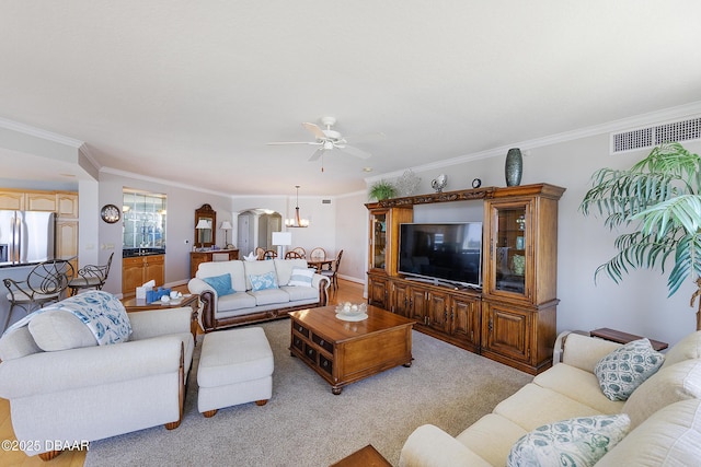 living area with ceiling fan with notable chandelier, arched walkways, light colored carpet, ornamental molding, and visible vents