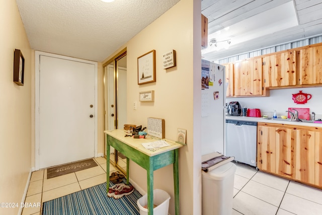 kitchen featuring stainless steel dishwasher, a textured ceiling, sink, light brown cabinets, and light tile patterned flooring