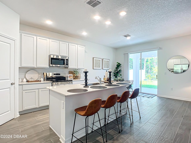 kitchen featuring a center island with sink, white cabinets, a breakfast bar area, wood-type flooring, and stainless steel appliances