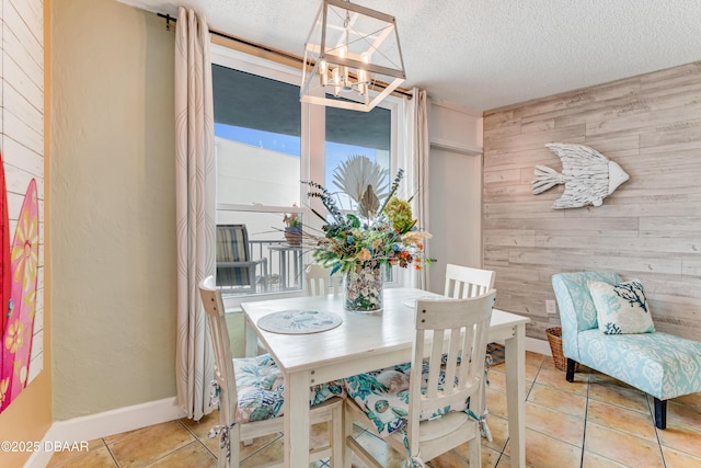 dining space featuring a textured ceiling, wood walls, light tile patterned flooring, and a chandelier