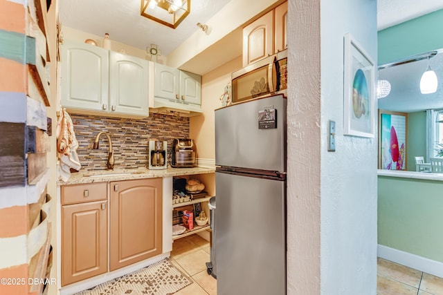 kitchen with light tile patterned floors, decorative backsplash, decorative light fixtures, freestanding refrigerator, and a sink