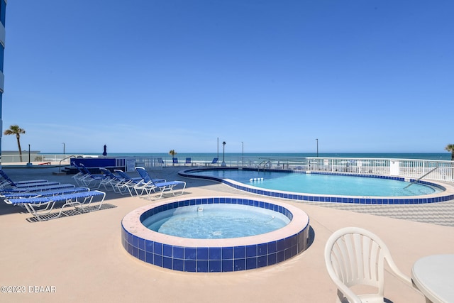 view of pool featuring a community hot tub, a water view, and a patio area