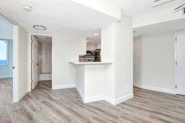 kitchen with white cabinets, light wood-type flooring, appliances with stainless steel finishes, and kitchen peninsula