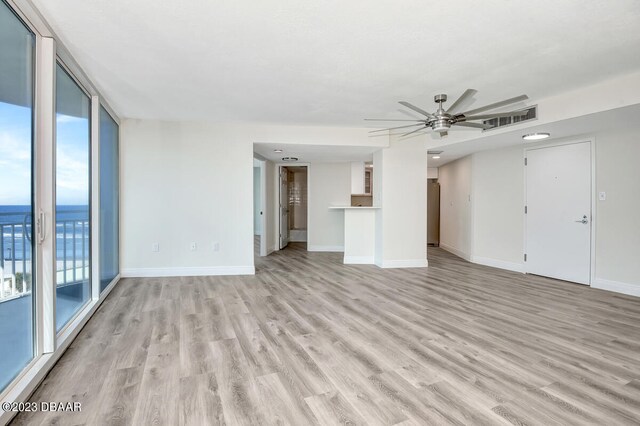 unfurnished living room featuring ceiling fan, a water view, light wood-type flooring, and a wall of windows