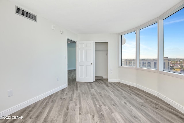 unfurnished bedroom with light wood-type flooring, multiple windows, and a closet