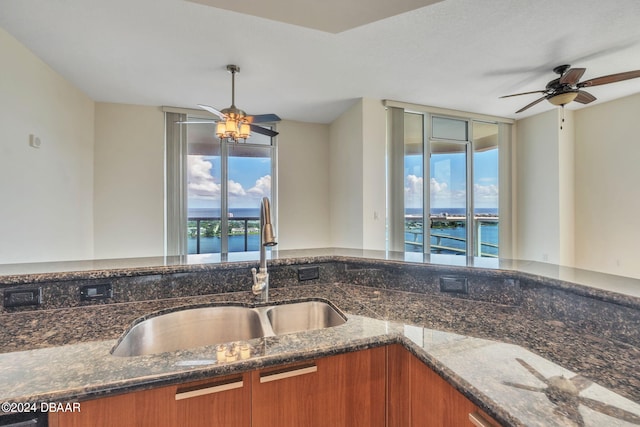 kitchen featuring ceiling fan, dark stone countertops, sink, and a water view