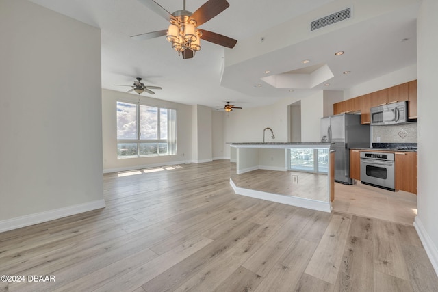 kitchen featuring appliances with stainless steel finishes, decorative backsplash, sink, light hardwood / wood-style floors, and ceiling fan