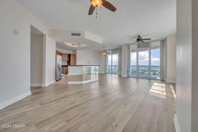 unfurnished living room with light hardwood / wood-style floors, ceiling fan, floor to ceiling windows, and sink