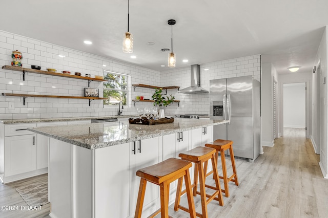 1703 Hill St, Edgewater, FL 32132 - kitchen with backsplash, light hardwood / wood-style flooring, white cabinets, stainless steel fridge, and wall chimney range hood
