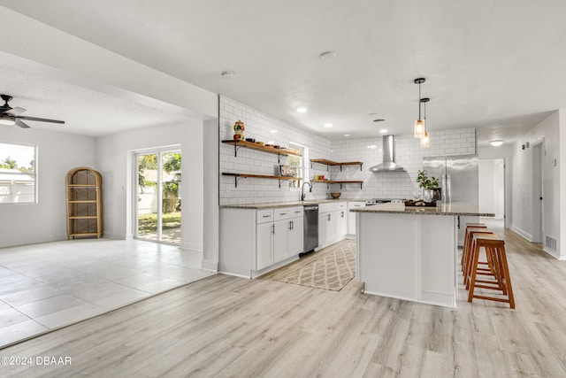 1703 Hill St, Edgewater, FL 32132 - kitchen featuring light hardwood / wood-style floors, a kitchen breakfast bar, wall chimney range hood, white cabinetry, and appliances with stainless steel finishes