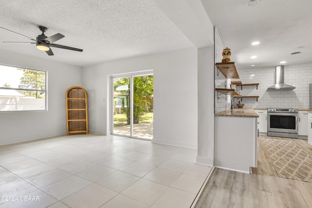 1703 Hill St, Edgewater, FL 32132 - interior space featuring white cabinetry, wall chimney exhaust hood, stainless steel electric stove, light hardwood / wood-style flooring, and decorative backsplash