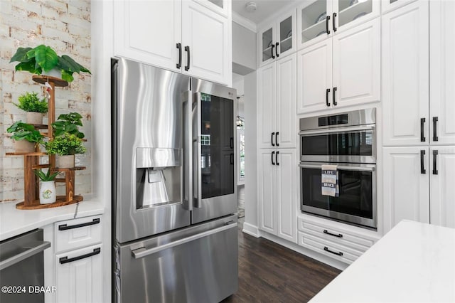 kitchen with appliances with stainless steel finishes, dark hardwood / wood-style flooring, white cabinetry, and brick wall