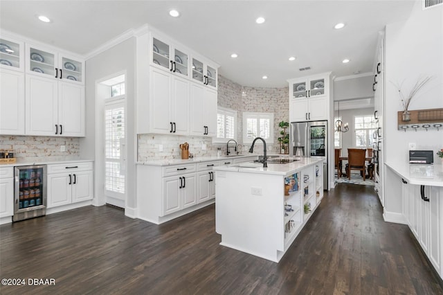 kitchen featuring white cabinetry, beverage cooler, plenty of natural light, an island with sink, and ornamental molding