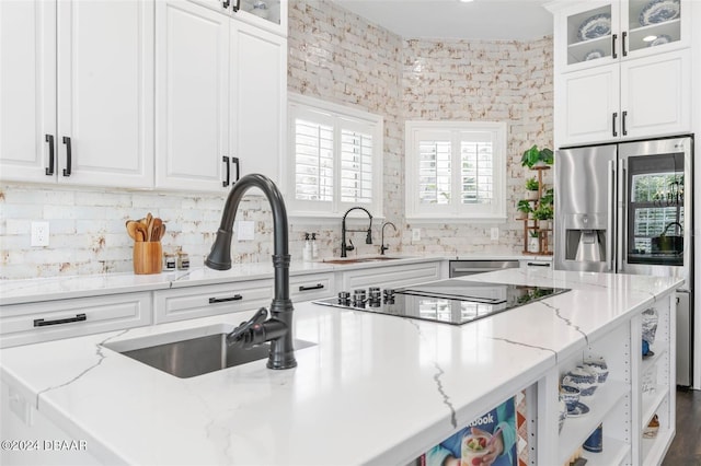 kitchen with stainless steel appliances, white cabinetry, sink, and light stone counters