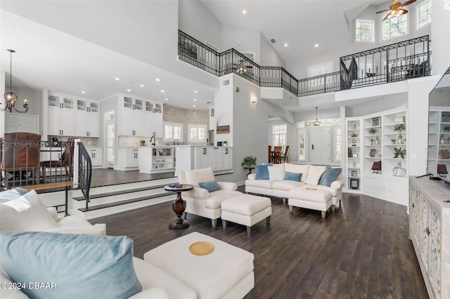 living room featuring ceiling fan with notable chandelier, a high ceiling, dark hardwood / wood-style flooring, and a wealth of natural light