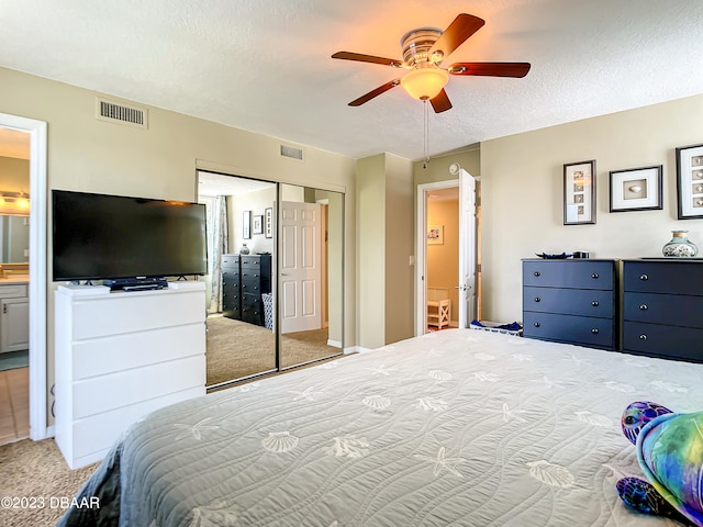 carpeted bedroom featuring a closet, a textured ceiling, ceiling fan, and ensuite bath