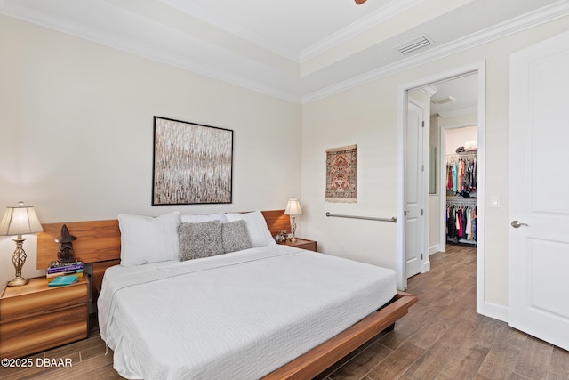 bedroom featuring wood-type flooring, a walk in closet, crown molding, and a closet