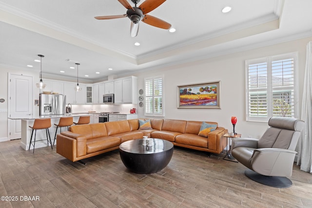 living room featuring a tray ceiling, wood-type flooring, and ornamental molding