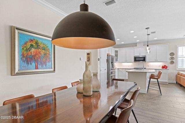 dining space featuring crown molding, sink, a textured ceiling, and light hardwood / wood-style floors