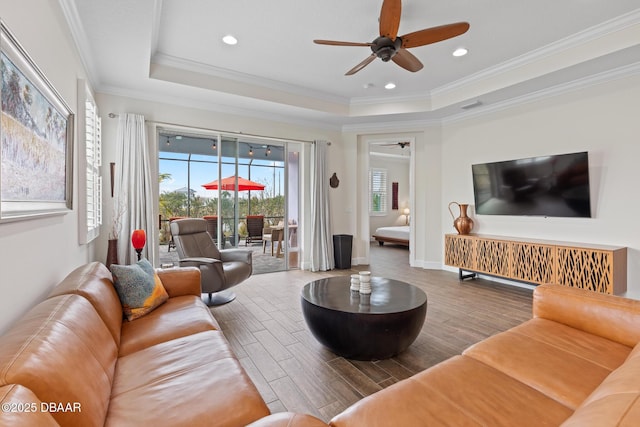 living room featuring wood-type flooring, ornamental molding, and a raised ceiling