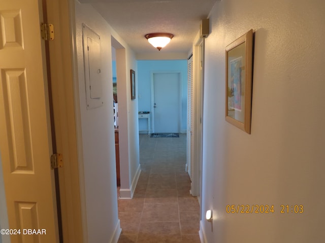 corridor with electric panel, a textured ceiling, and tile patterned floors