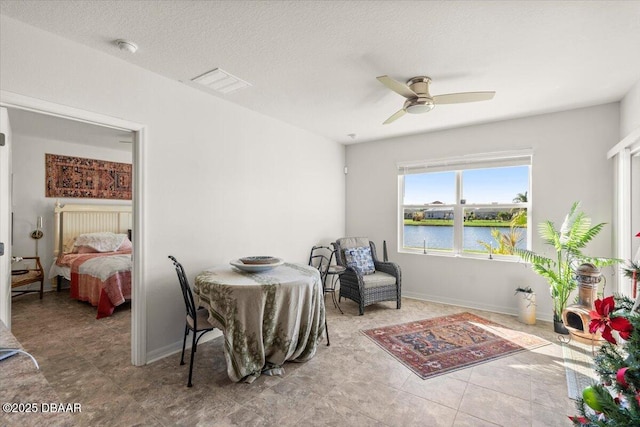 dining area featuring ceiling fan, a water view, and a textured ceiling