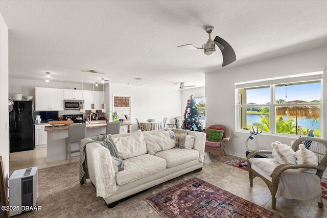 tiled living room with ceiling fan, a water view, and a textured ceiling