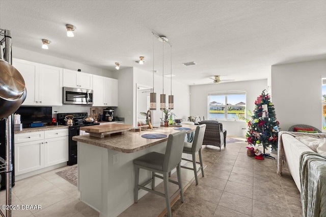 kitchen featuring sink, pendant lighting, a water view, black range with electric stovetop, and an island with sink