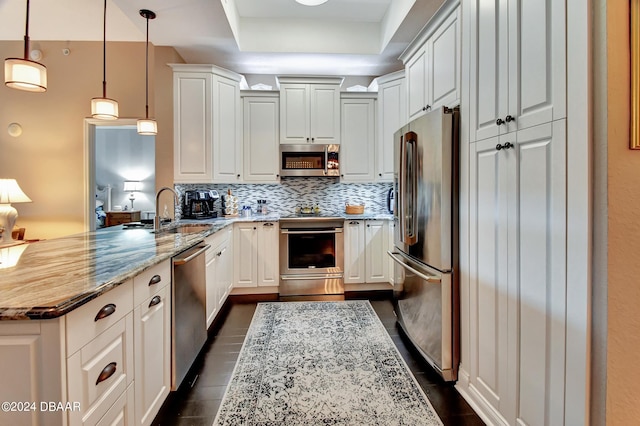 kitchen with light stone counters, white cabinetry, appliances with stainless steel finishes, hanging light fixtures, and sink