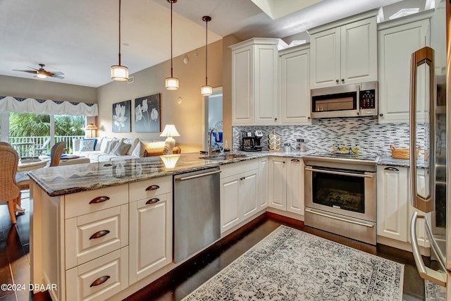 kitchen with stainless steel appliances, sink, kitchen peninsula, light stone countertops, and pendant lighting