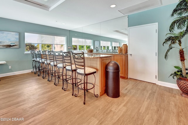 bar with light stone countertops, hanging light fixtures, and light wood-type flooring