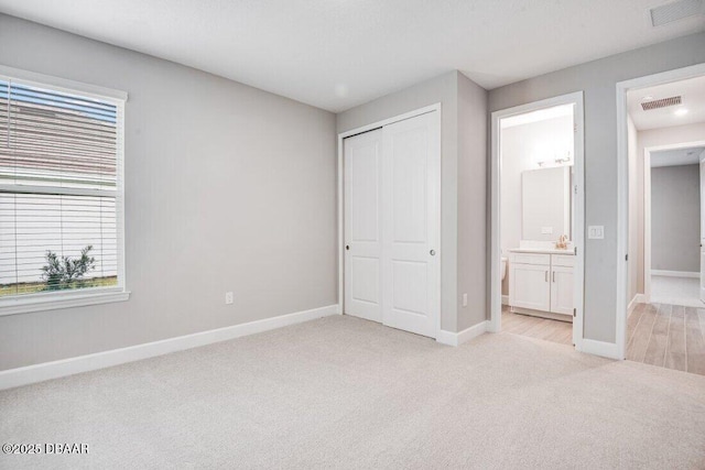 unfurnished bedroom with a closet, light carpet, and ensuite bath