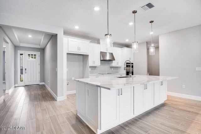 kitchen with white cabinetry, pendant lighting, a spacious island, and light stone counters