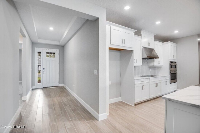 kitchen with light stone countertops, tasteful backsplash, black electric cooktop, light hardwood / wood-style floors, and white cabinetry