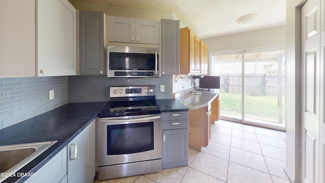 kitchen featuring appliances with stainless steel finishes, a textured ceiling, light tile patterned floors, backsplash, and gray cabinets